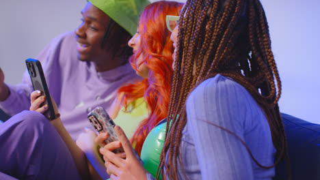 Close-Up-Studio-Shot-Of-Young-Gen-Z-Friends-Sitting-On-Sofa-Talking-And-Sharing-Social-Media-Post-On-Mobile-Phones-4